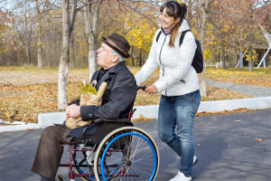 woman helping a disabled elderly man as she pushes his wheelchair